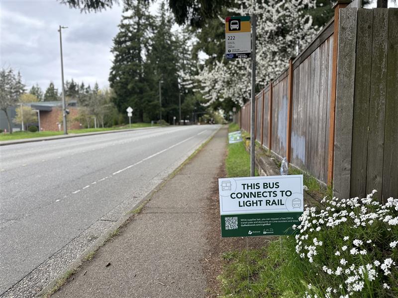 Bus stop with a 'this bus connects to light rail' yard sign